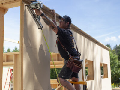 construction worker using a pneumatic nail gun to install wood fiber insulation boards on a wood frame house